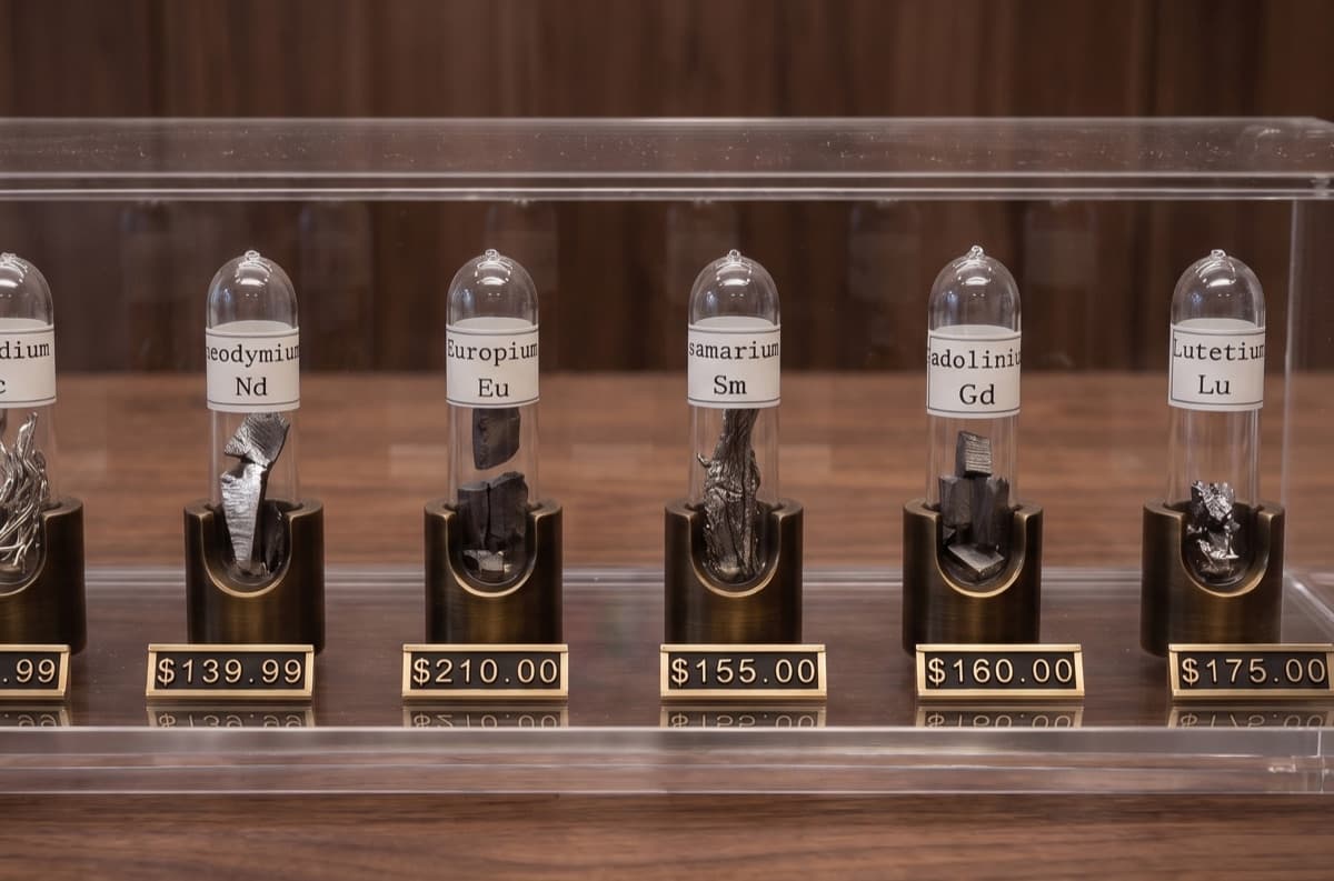 A glass display case of collector-grade rare earth metal samples sealed in labelled ampoules on brass stands, each with a retail price plaque (Nd, Eu, Sm, Gd, Lu).